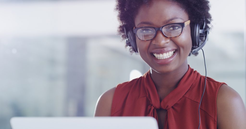Shot of young woman using a laptop and headset in a modern office